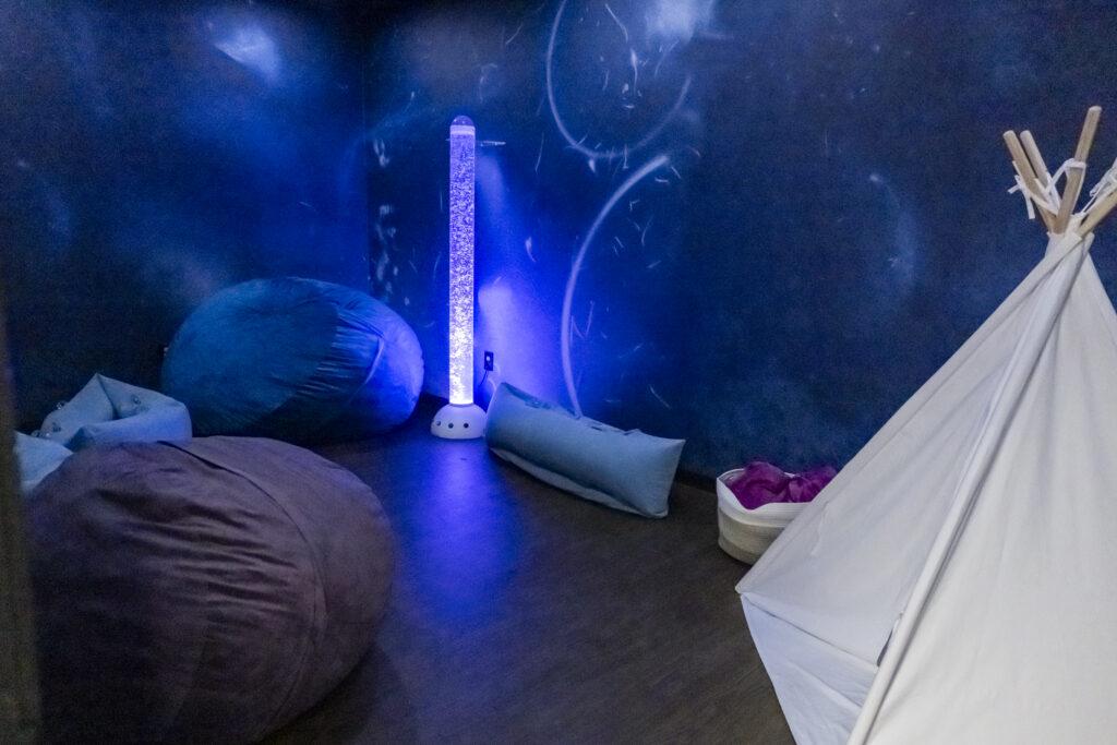 Darkened room with bean bag chairs, tent, and purple light