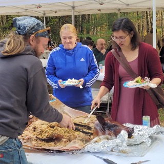 Guests fill their plates beside a whole roasted pig under the canopy at EdOpt’s 2026 Donor and Volunteer Appreciation Gathering.