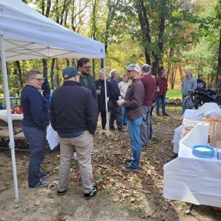 Guests talk in small groups beside the canopy and buffet tables at EdOpt’s 2026 Donor and Volunteer Appreciation Gathering.