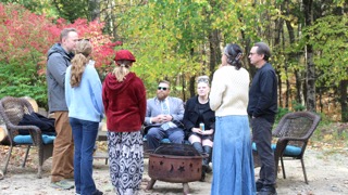 Guests stand and sit around a metal fire pit in an autumn woodland setting at EdOpt’s 2026 Donor and Volunteer Appreciation Gathering.