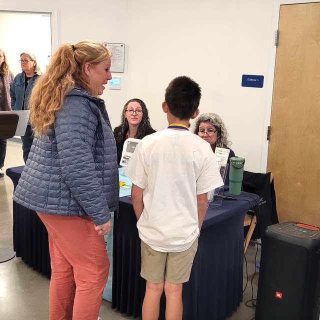 An adult and a child speak with EdOpt representatives at a table displaying education resources.