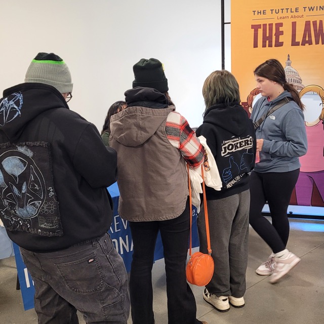 Young visitors gather at an information table beside a Tuttle Twins banner.