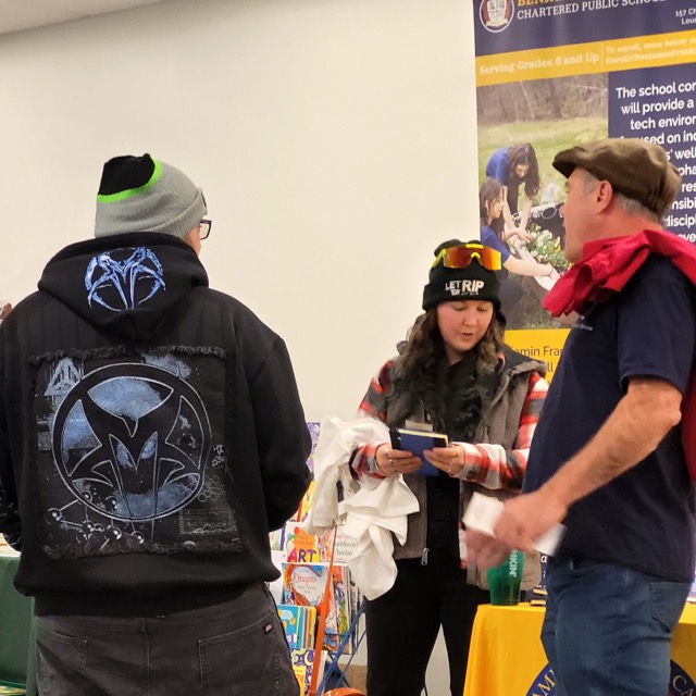 Visitors talk beside a Benjamin Franklin Academy banner while one reads printed materials.