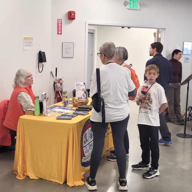 Visitors speak with a Benjamin Franklin Academy representative at a yellow-covered information table.