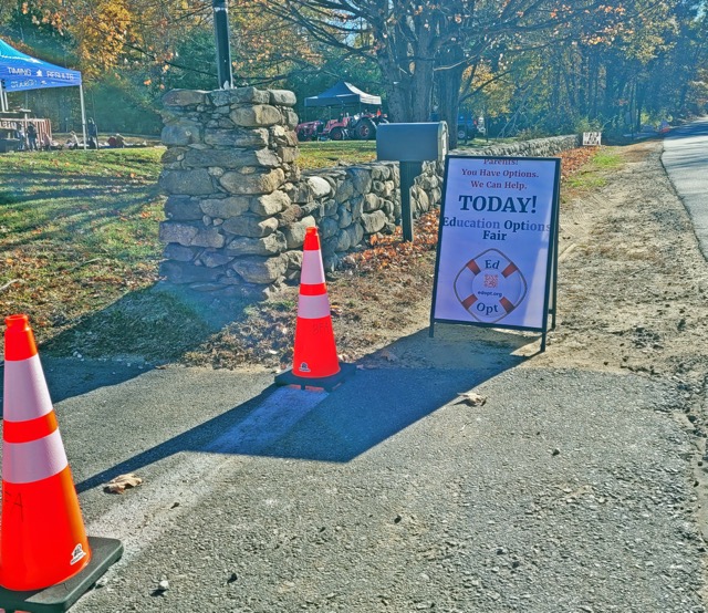 An EdOpt sign announces an education options fair beside traffic cones and a stone-lined driveway.