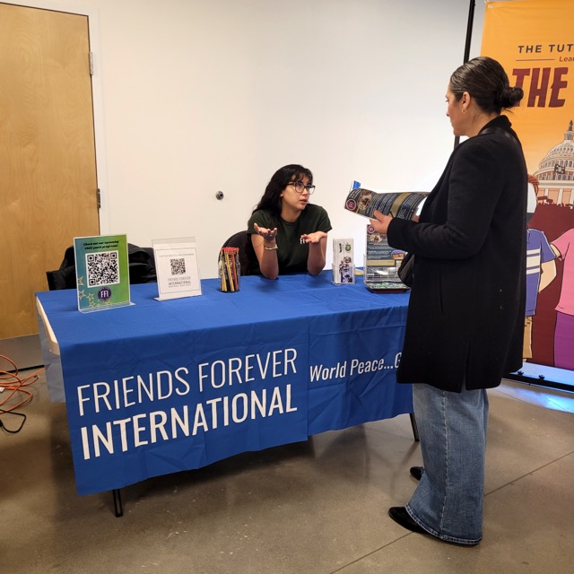 A Friends Forever International representative talks with a visitor holding a brochure at the organization’s table.