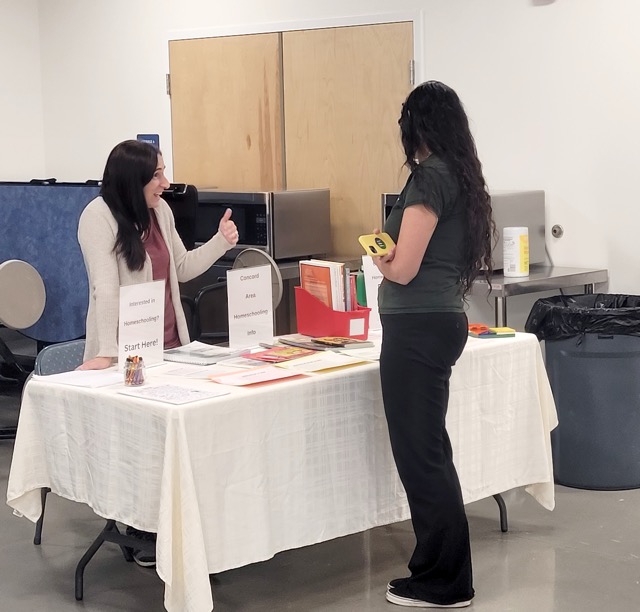 A homeschooling representative gestures while talking with a visitor at the Concord-area homeschooling table.