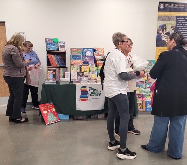Visitors talk beside a PaperPie display filled with colorful children’s books at the Loudon education fair.