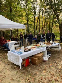 Guests gather beneath a white canopy behind an outdoor buffet table in an autumn yard.