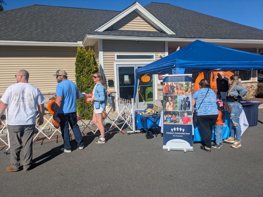 Parents standing at a tent and watching an event, near Children's Scholarship Fund tent