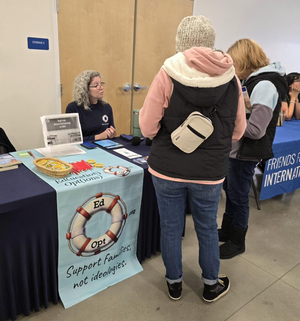 An EdOpt representative speaks with two visitors at a table displaying brochures and education resources.