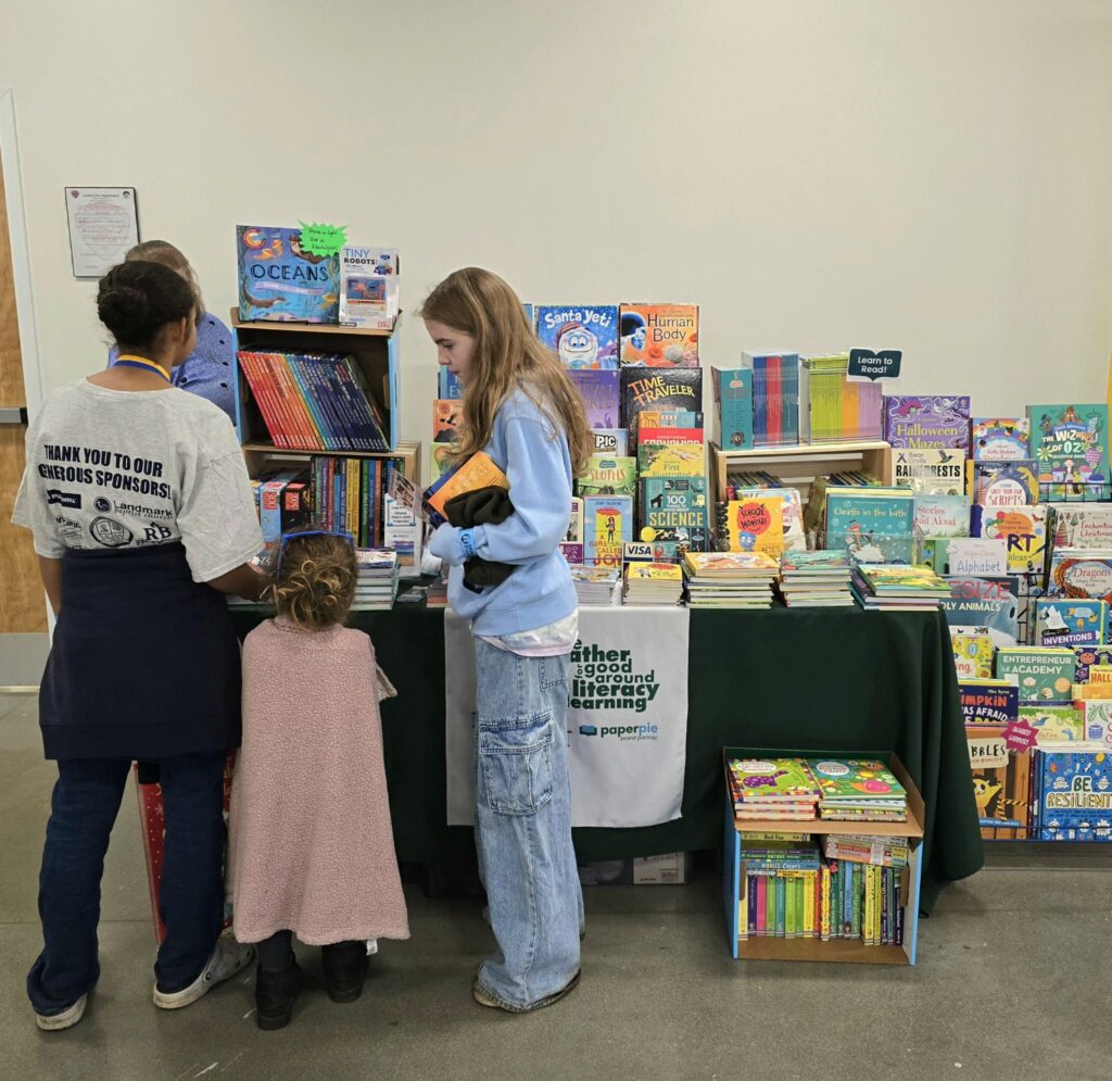 An adult and children browse colorful books at the PaperPie display during the Loudon education fair.